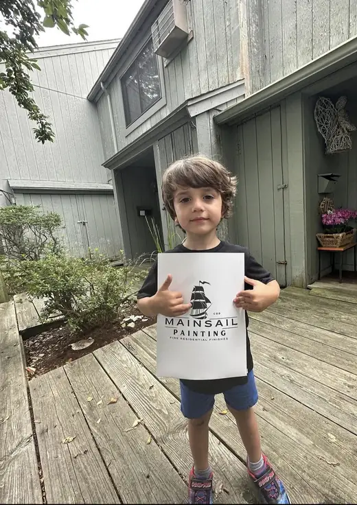 Filho do Vini segurando uma folha com a logo da Mainsail